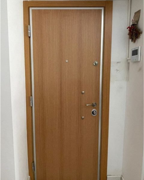 Puerta acorazada en madera clara con dos bombines y perfil de aluminio en un rellano