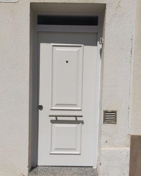 Puerta acorazada blanca de cuarterones con montante en una fachada