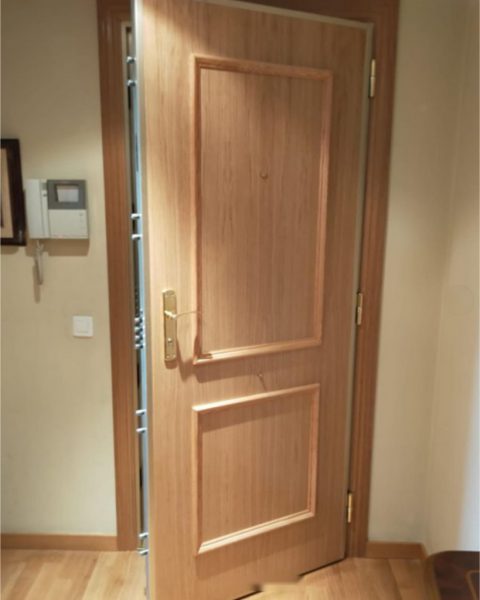 Puerta acorazada en madera con molduras, abierta, en un recibidor