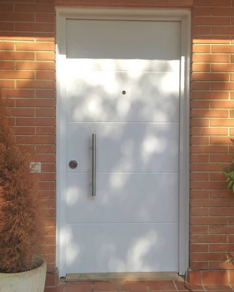 Puerta acorazada blanca con tirador vertical y montante en una fachada de ladrillo