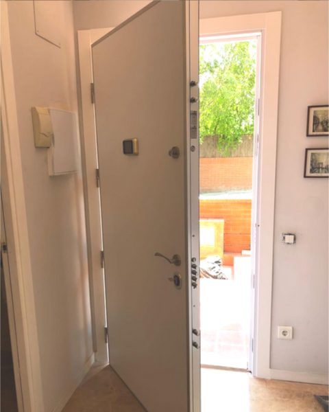 Puerta acorazada blanca abierta, con los bulones del canto a la vista