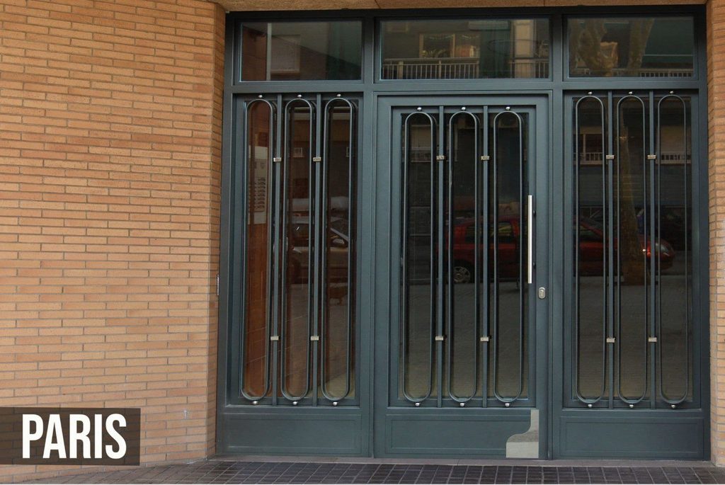 Puerta de portal modelo París, con óvalos dobles verticales sobre el vidrio de la hoja y de los fijos laterales, y montante de vidrio encima