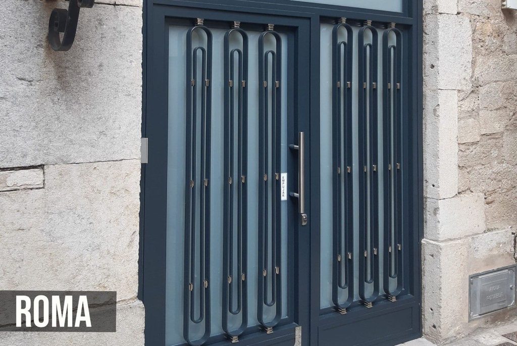 Puerta de comunidad modelo Roma, de dos hojas en gris antracita, con barrotes ovalados en forma de horquilla sobre vidrio mate y tirador vertical